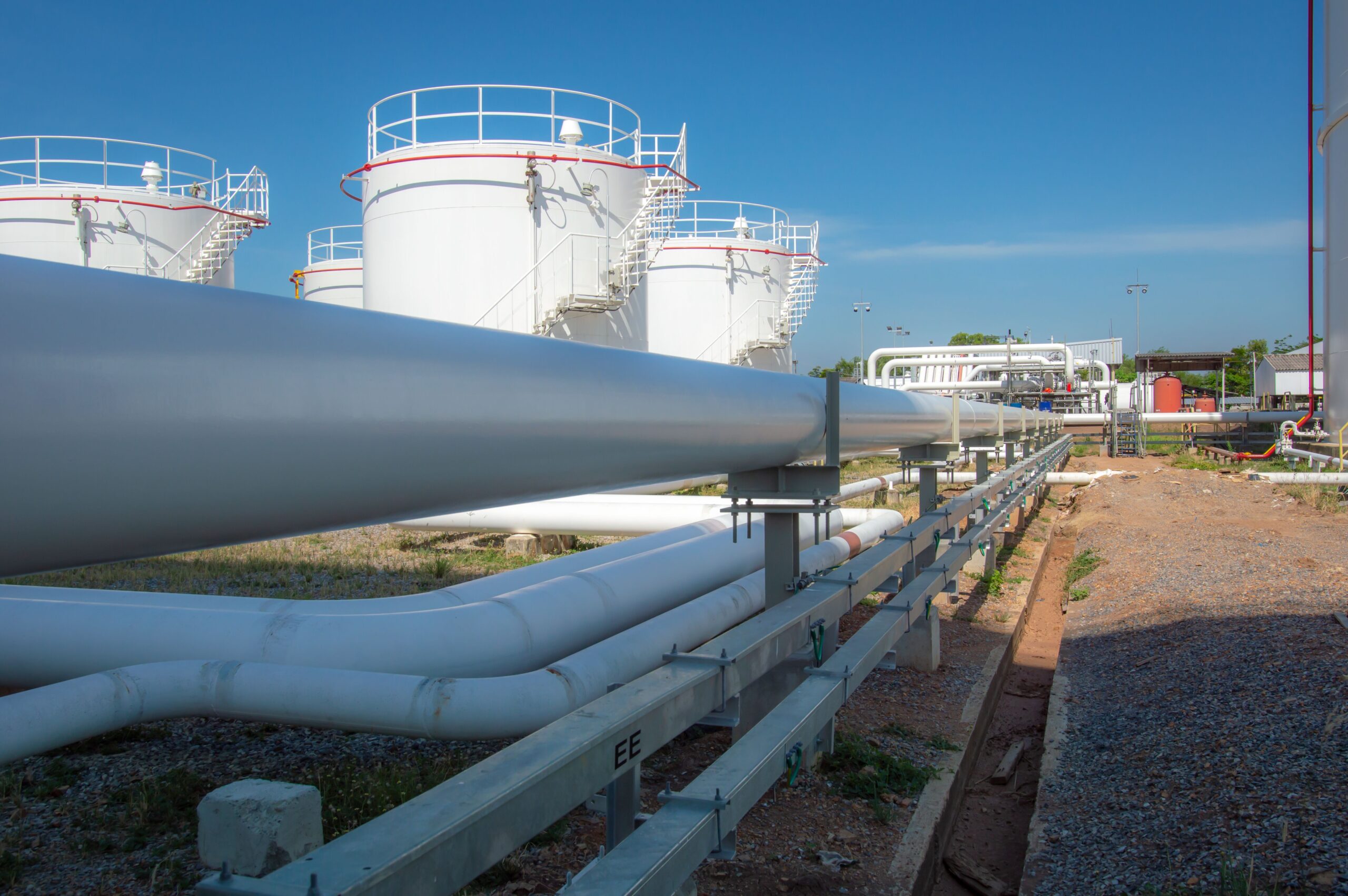 Pipelines run alongside storage tanks at an oil facility, highlighting infrastructure for liquid transport in the energy sector.